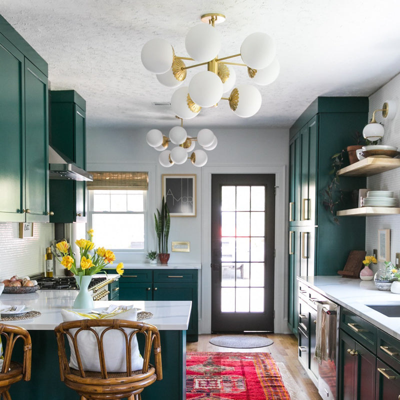 Kitchen featuring emerald green cabinets and globe cluster chandeliers, white island with rattan bar stools and a red runner rug