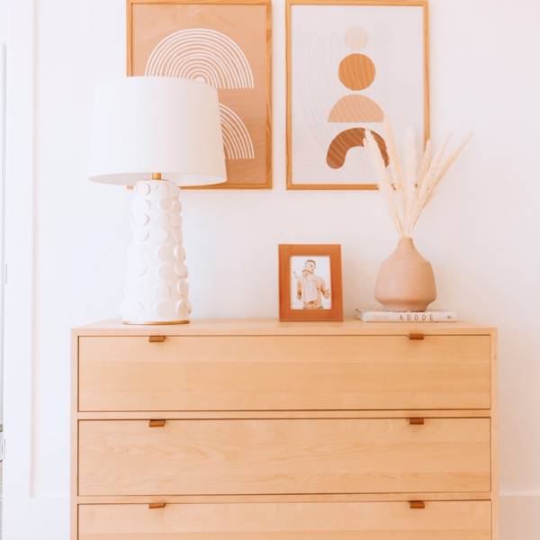 White textured table lamp on light wood dresser with framed abstract art and terracotta vase of pampas grass