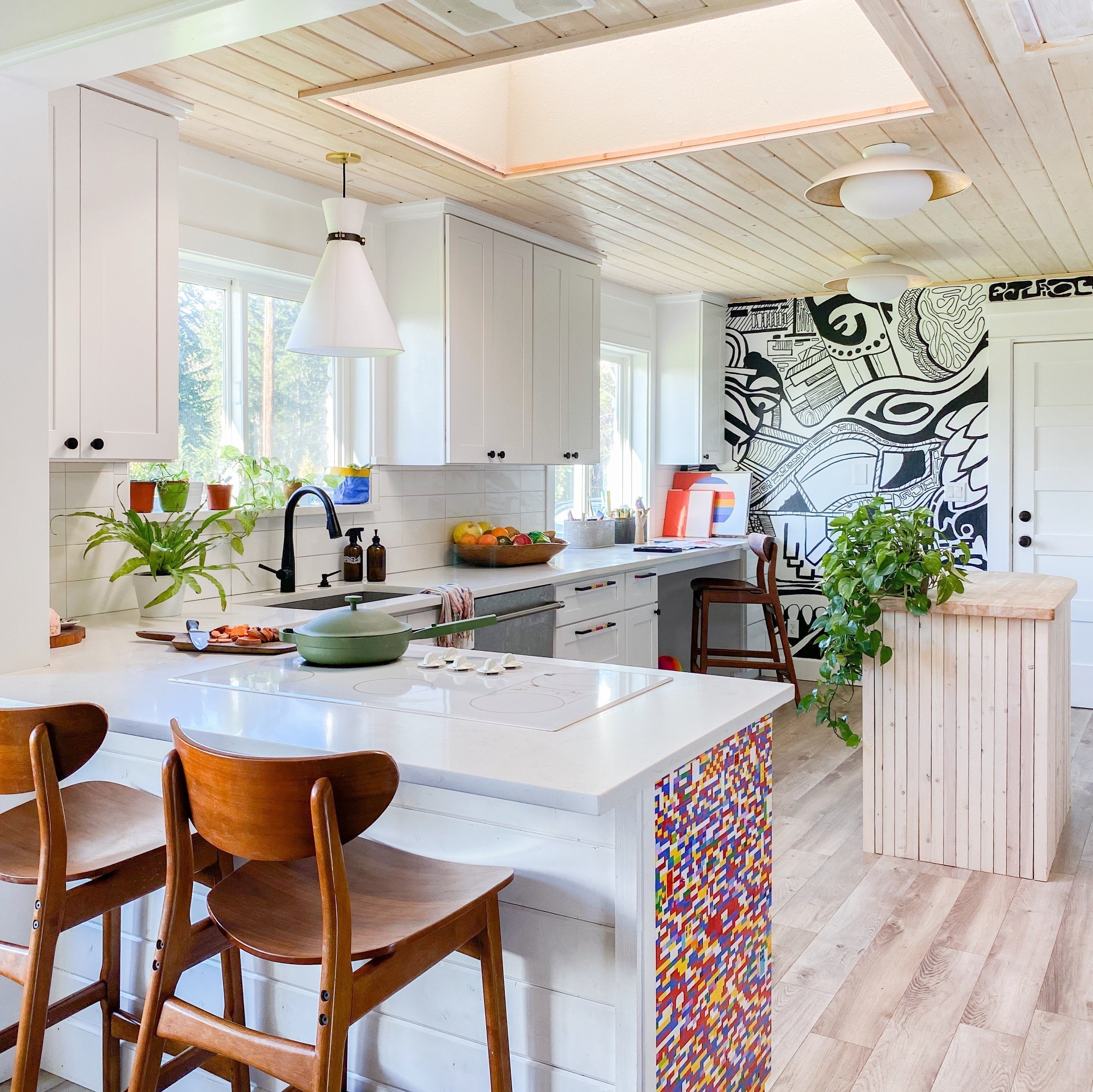 Kitchen featuring white cabinets and wood-plank ceiling, bold black-and-white mural on one wall, island with wooden stools