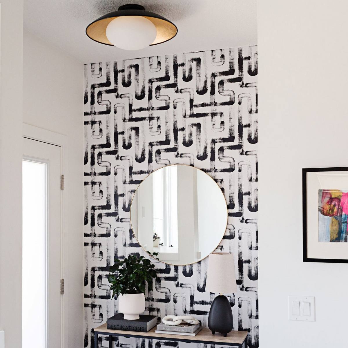 Entryway styled with black-and-white brushstroke wallpaper, round gold mirror, console table with potted plant, lamp, and decorative books