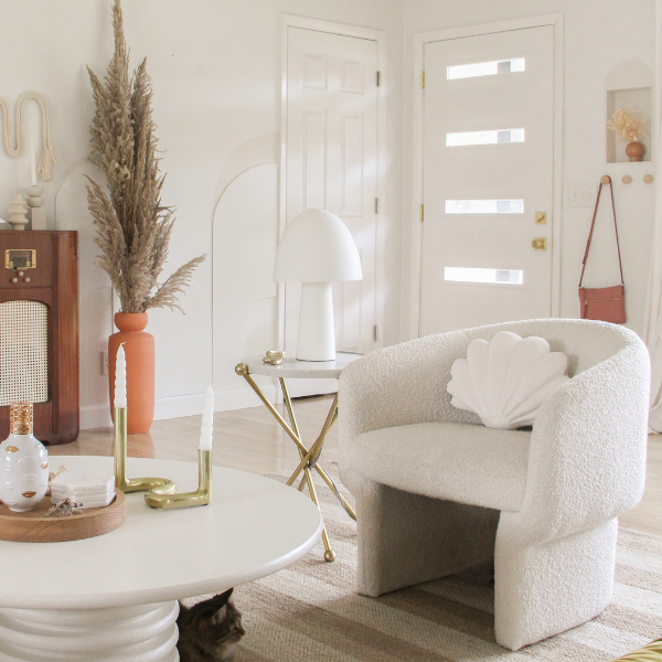 Cozy neutral living room with cream boucle shell armchair, round coffee table with brass candlesticks, pampas grass