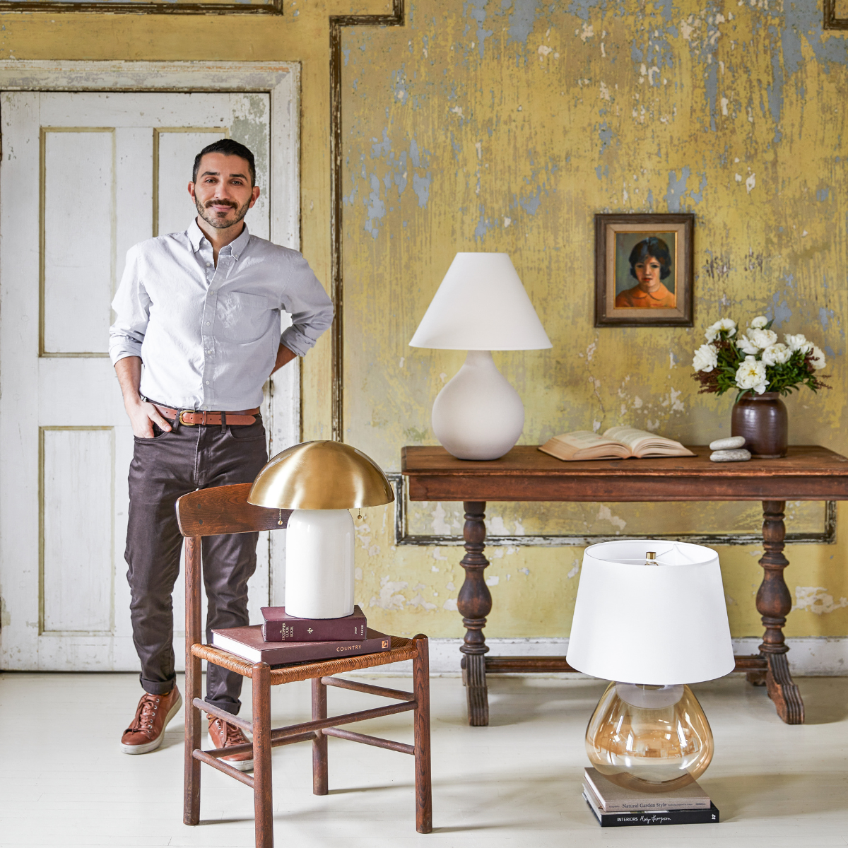 Man standing with hands in pockets beside a chair and table displaying Mitzi lamps in a vintage room