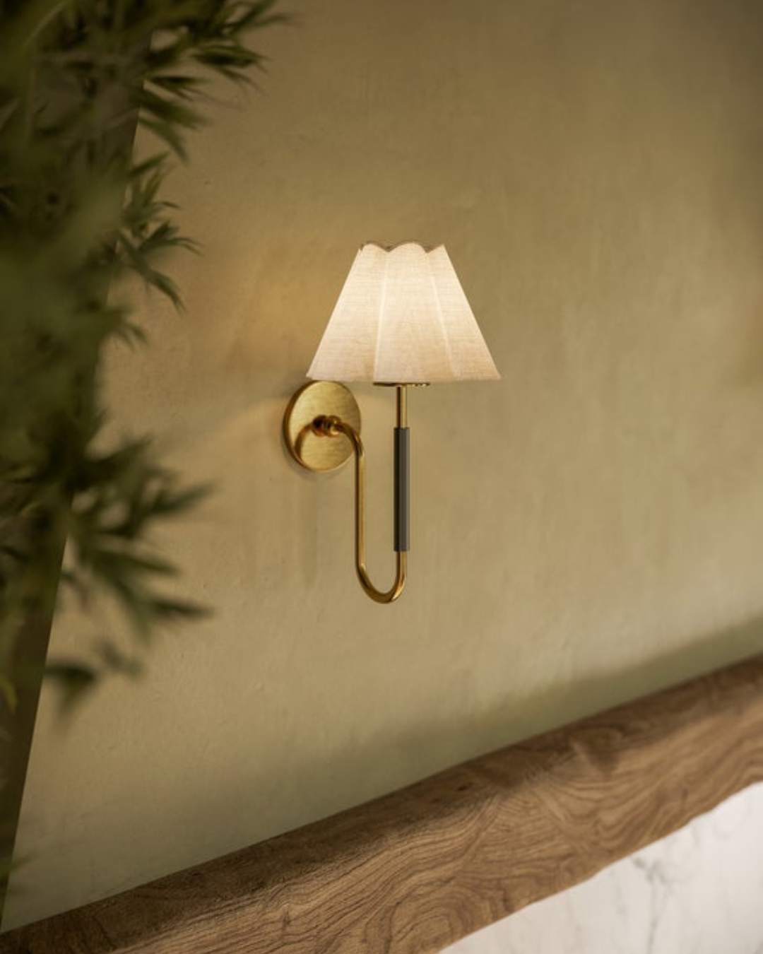 Side view of brass wall sconce with scalloped linen shade showcasing curved U-shaped arm and round backplate on a beige textured wall