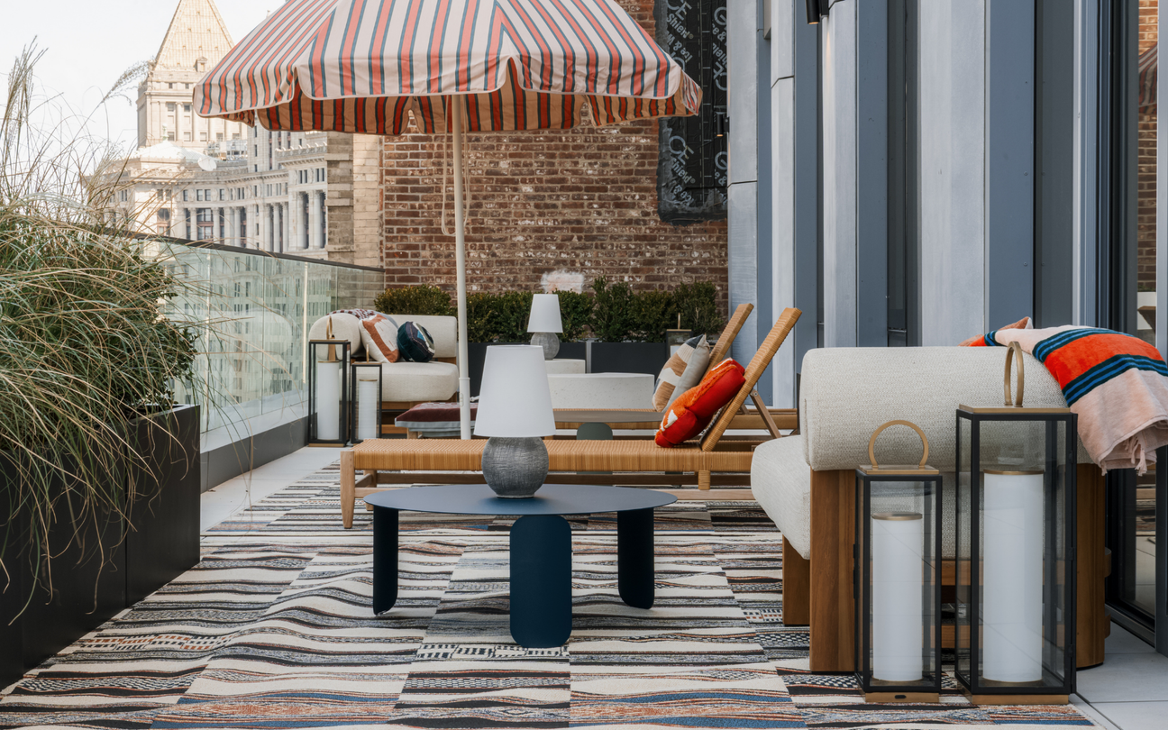 Rooftop patio with lounge seating, striped umbrella, tabletop lamp, and lanterns overlooking a city skyline
