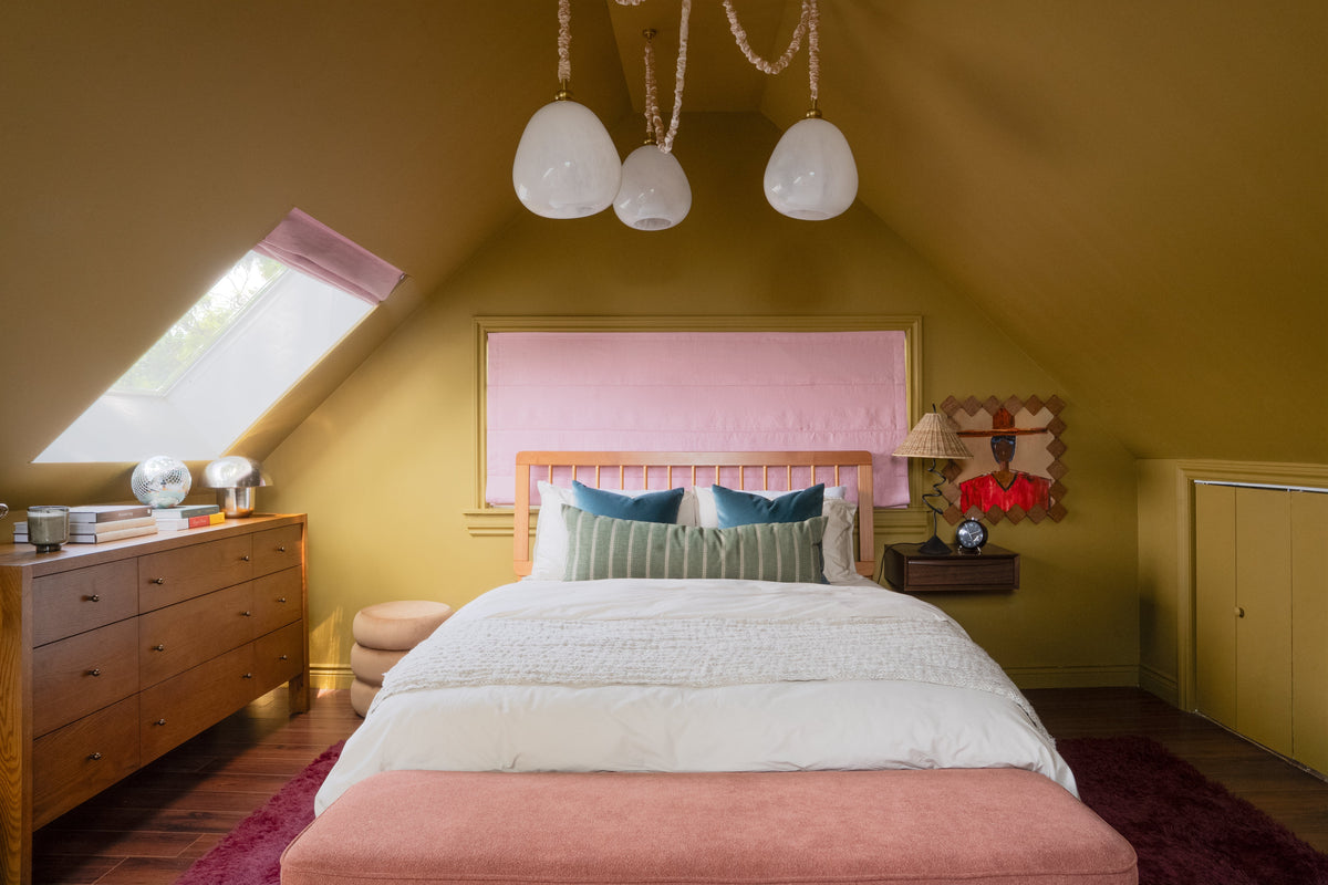 Bedroom decorated with olive green walls, pink window shade and bedding, wood dresser, and pendant lights