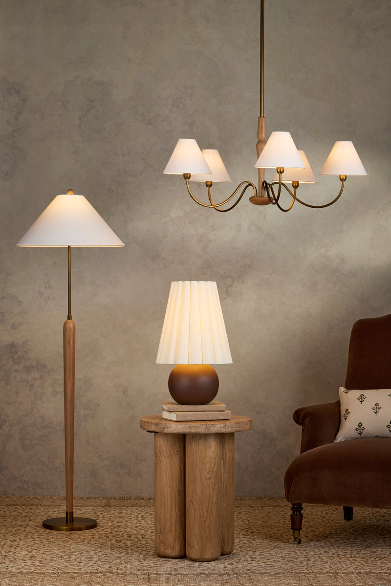 Lighting fixtures illuminate a styled room with a floor lamp, table lamp, chandelier, and brown armchair
