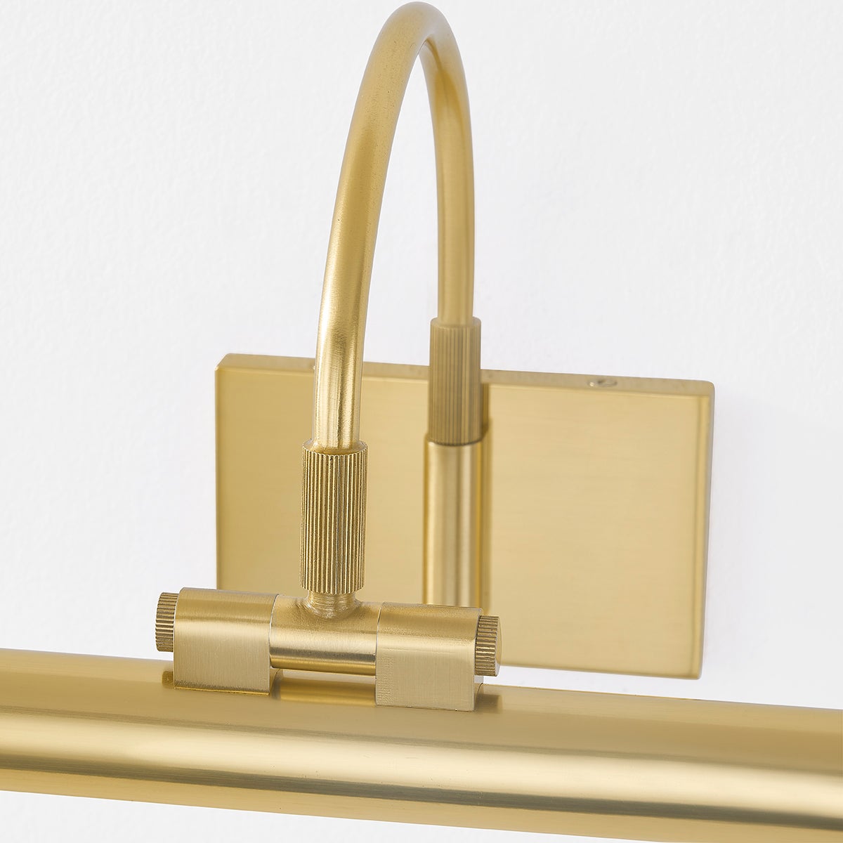 Close-up of Elowen Picture Light in aged brass showing adjustable curved arm, knurled fittings, and wall plate on white wall