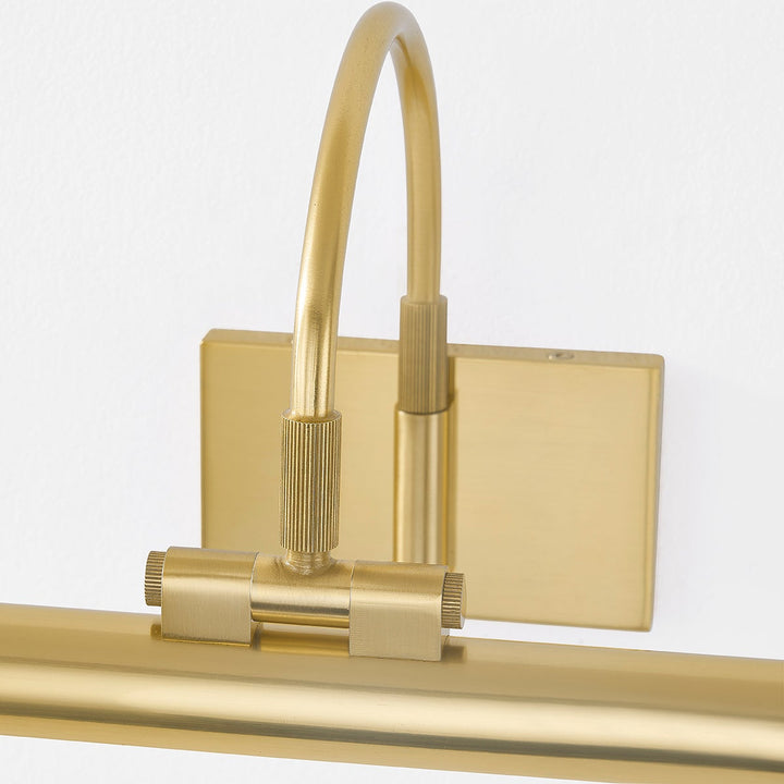 Close-up of Elowen Picture Light in aged brass showing adjustable curved arm, knurled fittings, and wall plate on white wall