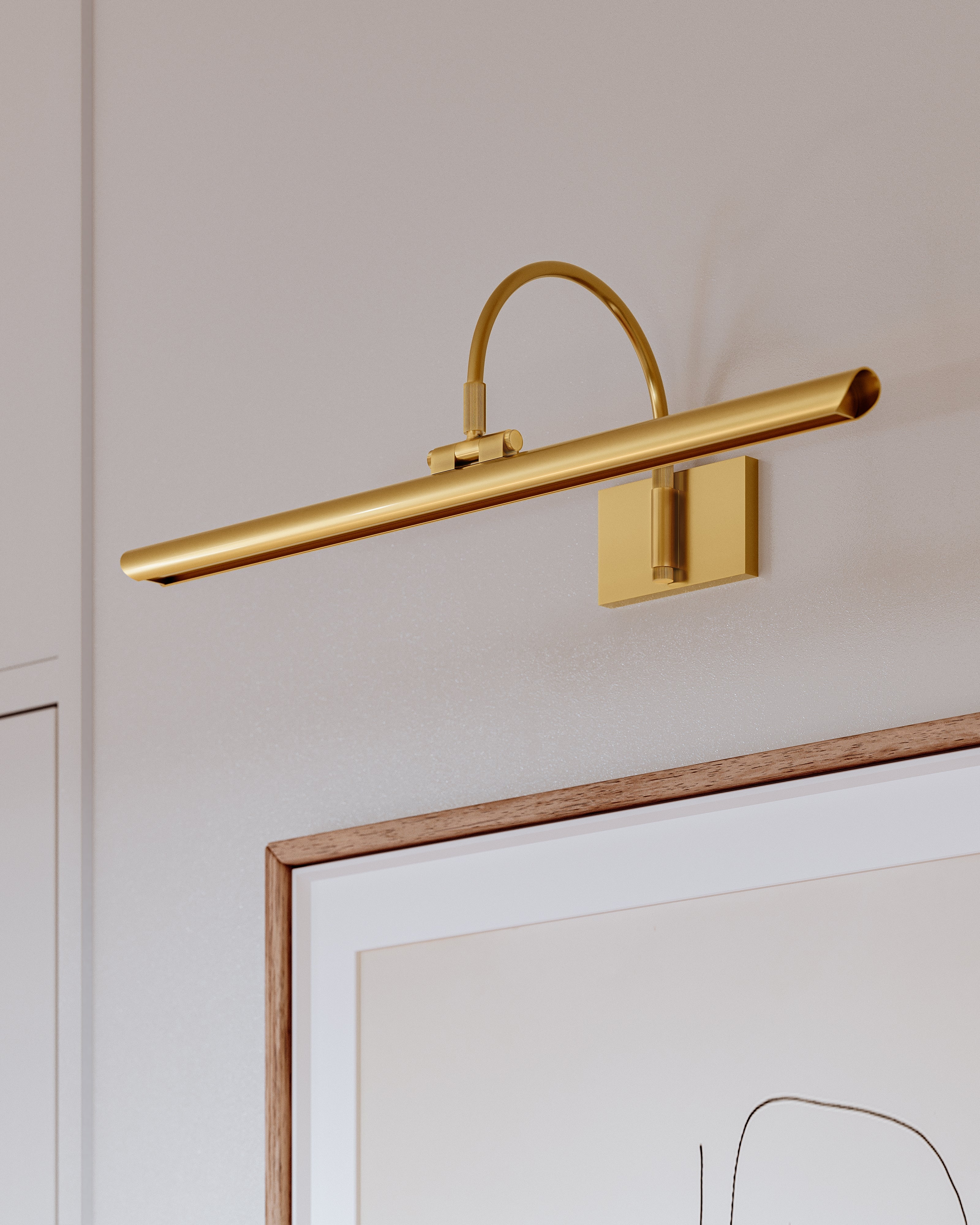 Close-up of Elowen Picture Light in aged brass showing curved arched arm and slim tubular shade mounted above framed artwork
