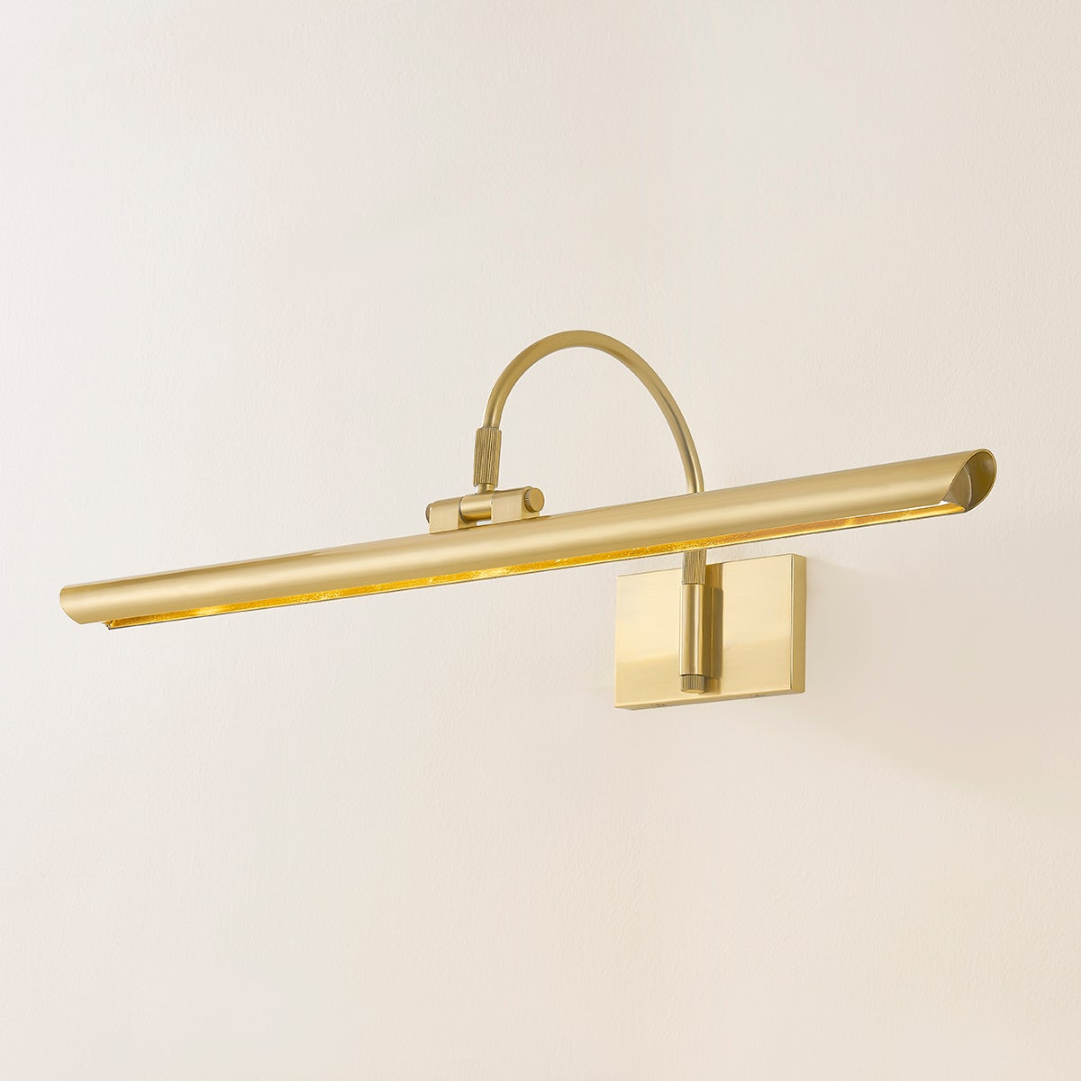 Angled view of Elowen Picture Light showcasing a long slim LED shade and curved arm in antique gold finish against pale wall