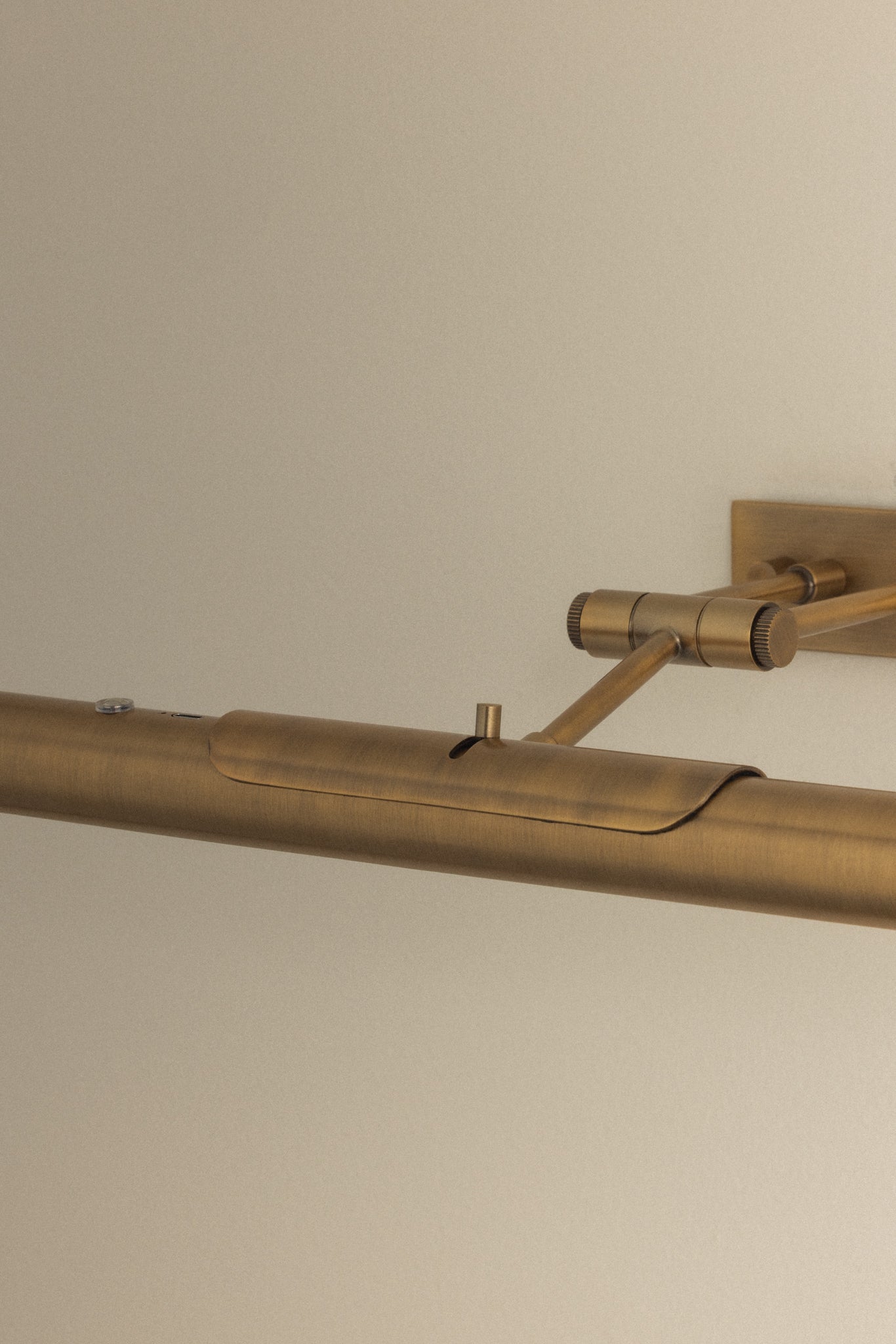 Close-up of Kenya Rechargeable Picture Light showcasing adjustable double-arm hinge and Patina Brass finish on a neutral wall