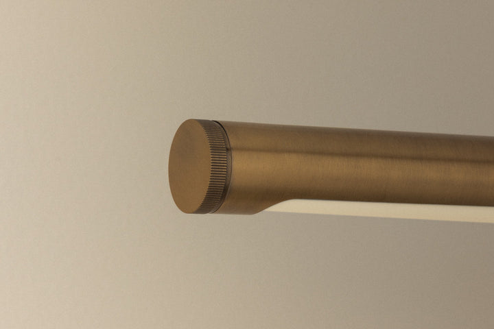 Close-up of Kenya Rechargeable Picture Light showing end cap and knurled adjustment ring in Patina Brass against a neutral wall